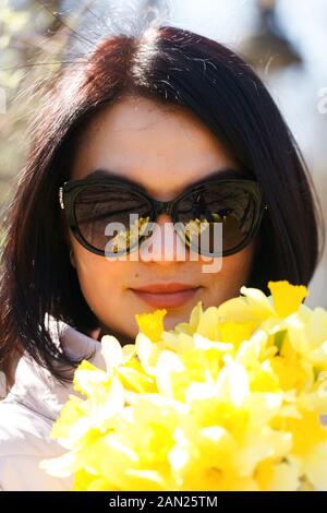 Une belle jeune fille brune à lunettes tenant un bouquet de jonquilles. Close up portrait of beautiful girl holding bouquet de rsp jaune vif Banque D'Images