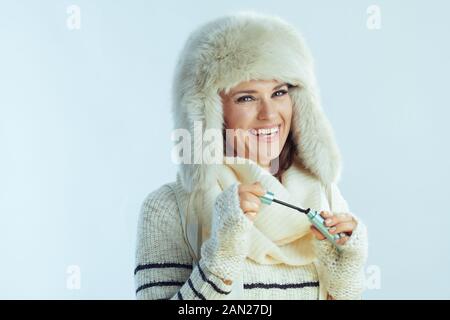 Portrait d'une femme souriante à la mode dans un pull blanc rayé, un foulard et des rabats d'oreille chapeau à l'aide de mascara sur fond bleu clair d'hiver. Banque D'Images