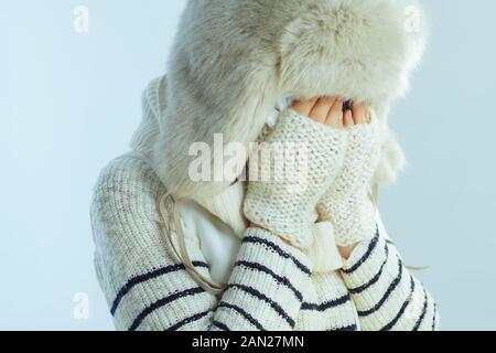 triste femme moderne en pull blanc rayé, écharpe et rabats d'oreille chapeau pleurant isolé sur fond bleu clair d'hiver. Banque D'Images