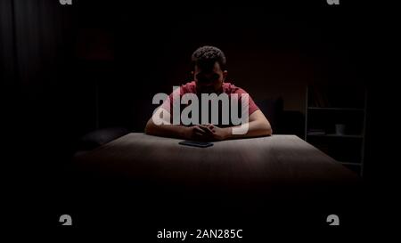 Déprimé seul homme assis dans une pièce sombre à la recherche au téléphone, en attente d'appel Banque D'Images