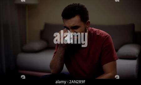 Jeune homme Overemotional soap opera regarder à la maison et pleurer, essuyant des larmes Banque D'Images