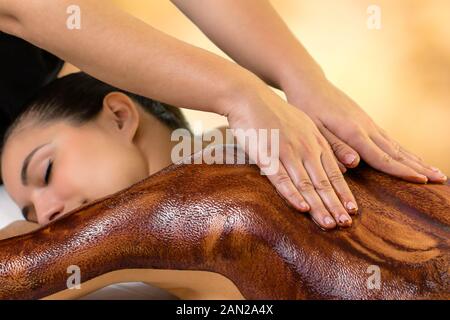 Vue latérale du cacao chaud faisant mains massage sur femme. Chocolat noir propagation thérapeute cire sur le dos de la femme. Banque D'Images