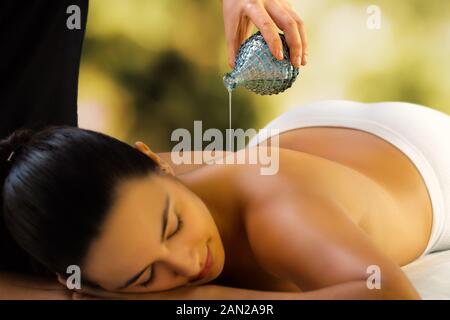 Close up of woman relaxing in spa thérapeute de faible luminosité.verser l'huile de massage sur le dos. Banque D'Images