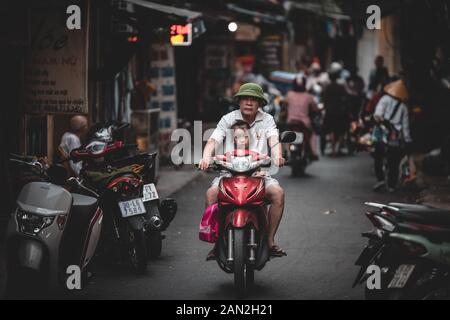 Hanoi, Vietnam - 18 octobre 2019 : Un vieil homme monte un scooter à travers les rues du Vietnam avec une petite fille à l'avant Banque D'Images