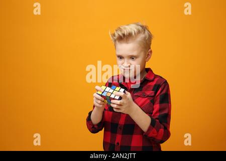 Un jeune garçon jouant avec un jouet. Jeune beau garçon caucasien souriant dans la chemise rouge sur fond jaune. Horizontale, droite. Banque D'Images