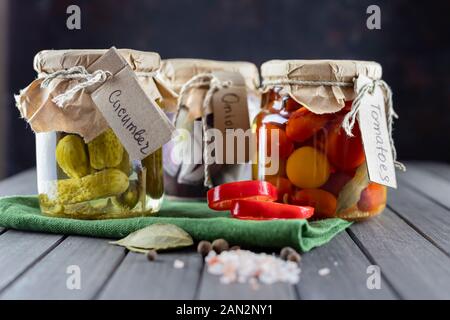 Trois pots de verre de concombres fermentés, tomate, oignons, piment, épices, sel. des légumes sur un fond sombre. à l'aide de vert textile. fermentatio Banque D'Images