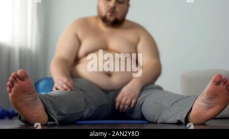 L'excès de l'homme se reposant après les exercices d'étirement assis sur le tapis de fitness Banque D'Images