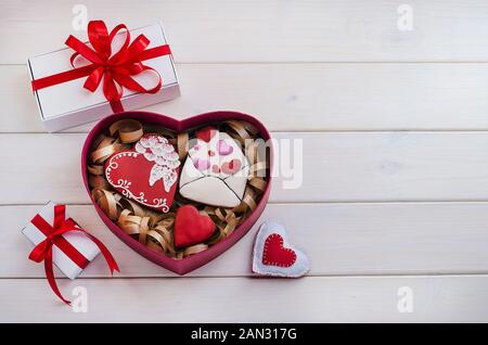 Les sucreries comme cadeau pour la Saint-Valentin. Gingerbread cookies en forme de cœur et une enveloppe avec des cadeaux blancs avec rubans rouges avec l'exemplaire de l'espace sur un Banque D'Images