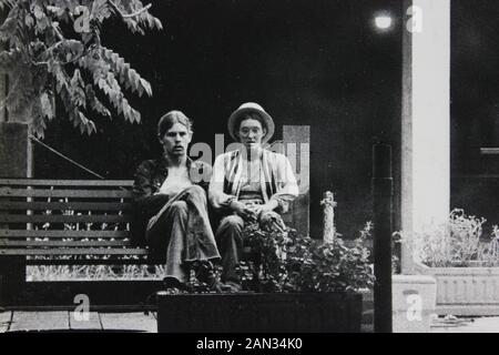 Photographie noir et blanc des années 70 de deux hommes assis sur un banc de parc Banque D'Images