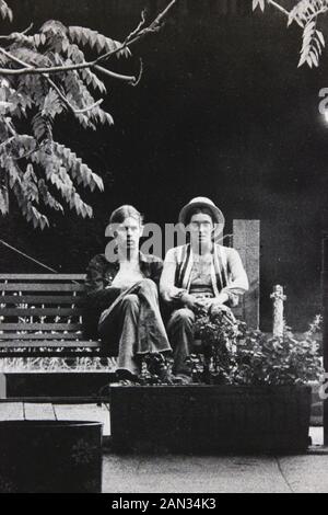 Photographie noir et blanc des années 70 de deux hommes assis sur un banc de parc Banque D'Images