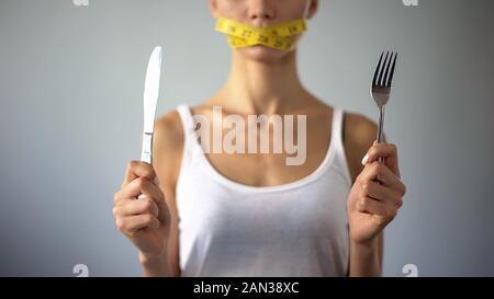 Fille anorexique holding fourchette et couteau, bouche fermée avec de la bande, restrictions Banque D'Images