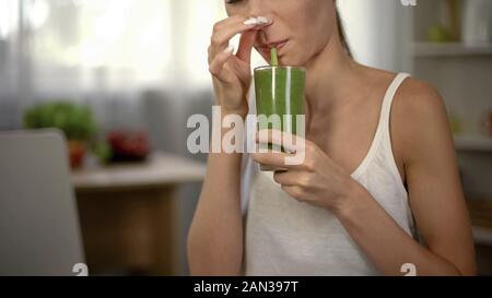 Woman drinking smoothie vert dégoûtant, fermeture de nez, de mauvaise odeur et goût Banque D'Images