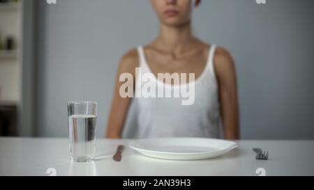 Fille anorexique assis en face de la plaque vide, l'eau potable, diète sévère Banque D'Images