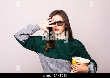 Jeune fille effrayée dans des lunettes imax en relief couvrant le visage avec la paume, regarder un film, tenant un seau de popcorn isolé sur fond blanc. Banque D'Images