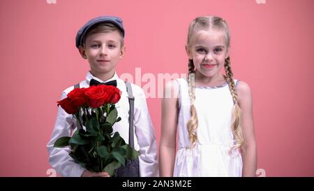 Jeune fille souriante et son petit copain holding fleurs rouges, à la recherche d'appareil photo Banque D'Images