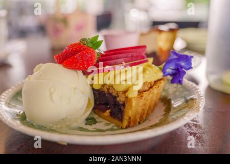 Vue sur le gâteau à tarte aux baies en miettes de pomme avec glace à la vanille sur le dessus avec fraise. Banque D'Images