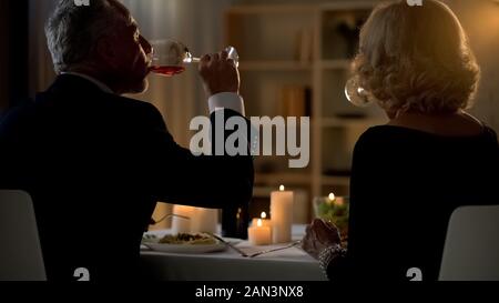 Vieux couple drinking red wine pendant un dîner romantique, les traditions familiales, l'amour Banque D'Images
