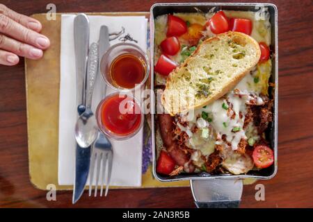 Petit déjeuner asiatique fusion, œufs frits servis sur la poêle avec du porc râpé sec, du fromage, du pain à l'ail et des tomates fraîches, et sauce au ketchup sur le côté. Banque D'Images