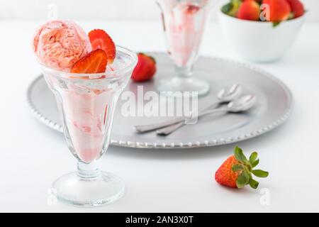Un plat de dessert en verre rempli de la crème glacée aux fraises avec un autre sur un plateau de métal à l'arrière. Banque D'Images