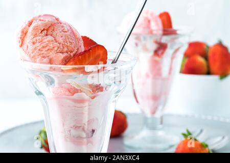 Un gros plan d'une fraise à la crème glacée avec une autre à l'arrière et un bol de fraises. Banque D'Images