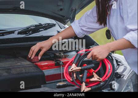 De gros plan femme main tenant le fil de cuivre du câble de batterie pour la réparation de voiture cassée par brancher la batterie avec la ligne rouge et noir à la borne électrique par il Banque D'Images