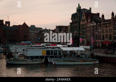 Les bateaux d'excursion attendent à Damrak à Amsterdam alors qu'ils se préparent à prendre des gens pour des visites sur les canaux autour de la ville Banque D'Images