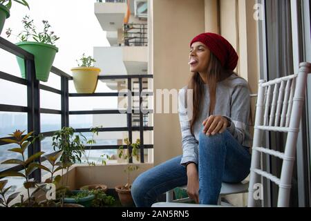 Jeune fille de mâcher de la gomme tout en étant assis sur le balcon à la maison. (Enfants) Banque D'Images