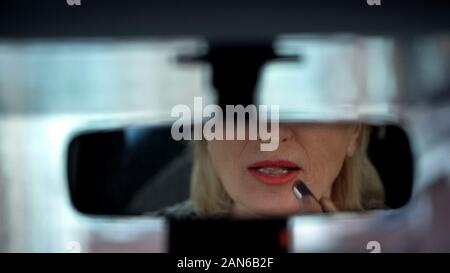 Femme d'appliquer le rouge à lèvres et à la recherche en vue arrière miroir de voiture Banque D'Images