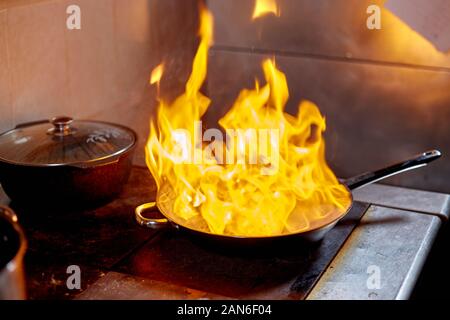 Flambe. Feu dans la poêle à frire. Chef professionnel dans une cuisine commerciale. Faites frire des aliments dans une poêle moulante sur la table de cuisson dans la cuisine extérieure Banque D'Images