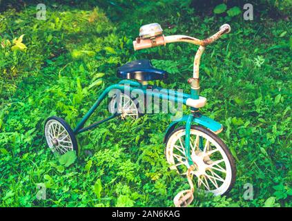 Ancienne rétro rusty children's tricycle debout sur l'herbe verte Banque D'Images