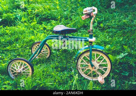 Ancienne rétro rusty children's tricycle debout sur l'herbe verte Banque D'Images