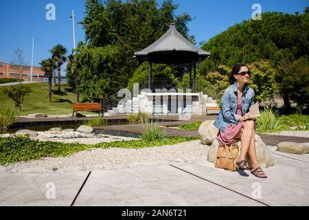 Femme assise sur un parc et à écrire ou à dessiner sur son ordinateur portable Banque D'Images