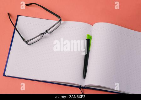 Journal vierge, stylo et verres sur fond rose. Espace libre pour le texte. Travail de bureau. Banque D'Images