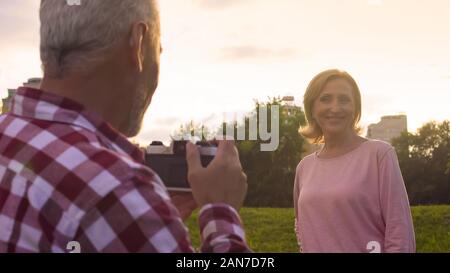 Un homme âgé à faire des photos de sa belle épouse dans le parc au coucher du soleil, la date, les passe-temps Banque D'Images