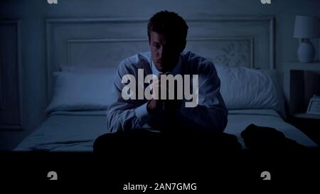 Hâte beau mâle en tailleur assis sur le lit, se frottant les mains, des problèmes Banque D'Images