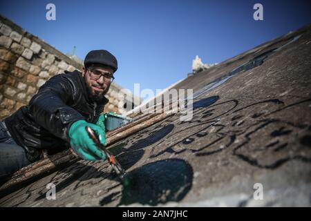 Kafr Nabî, la Syrie. 15 Jan, 2020. Une photo disponible le 16 janvier 2020 montre l'artiste syrien Abu Malik Al-Shami dessiner une fresque graffiti sur le mur d'un bâtiment qui a été détruit dans un bombardement. Al-Shami a commencé à peindre des murales retour en 2014 sur les murs de l'a détruit des bâtiments de sa ville natale assiégée puis de Darayya, situé à au sud-ouest de Damas. Après son déplacement, l'artiste a continué à peindre des murales à Idlib pour attirer l'attention sur la situation humanitaire catastrophique. Credit : Anas Alkharboutli/dpa/Alamy Live News Banque D'Images