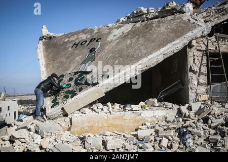 Kafr Nabî, la Syrie. 15 Jan, 2020. Une photo disponible le 16 janvier 2020 montre l'artiste syrien Abu Malik Al-Shami dessiner une fresque graffiti sur le mur d'un bâtiment qui a été détruit dans un bombardement. Al-Shami a commencé à peindre des murales retour en 2014 sur les murs de l'a détruit des bâtiments de sa ville natale assiégée puis de Darayya, situé à au sud-ouest de Damas. Après son déplacement, l'artiste a continué à peindre des murales à Idlib pour attirer l'attention sur la situation humanitaire catastrophique. Credit : Anas Alkharboutli/dpa/Alamy Live News Banque D'Images