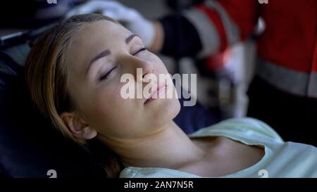 Femme pâle allongée, inconsciente, gros plan sur une civière pour prodiguer les premiers soins paramédicaux Banque D'Images