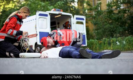 Les ambulanciers fournissant des soins médicaux d'urgence à l'homme sur la route, victime d'un accident de voiture Banque D'Images
