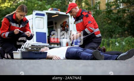 Aider les ambulanciers homme inconscient sur la route, faisant de l'injection de l'insuline Banque D'Images