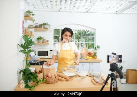 Jolie jeune femme d'origine asiatique food blogger travaille sur une nouvelle vidéo et d'expliquer comment cuisiner un plat Banque D'Images