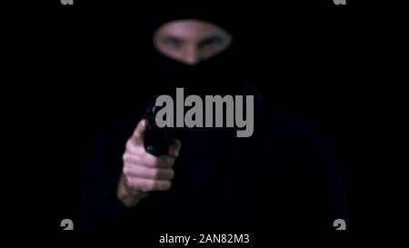 Silhouette de casier à balaclava visant à main armée d'armes à feu, fond noir Banque D'Images