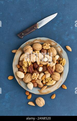 Mélange de noix sur une plaque - noix, amandes, noix de pécan, macadamia. La nourriture végétalienne saine. Nettoyer l'alimentation saine, équilibrée. Tableau lumineux bleu pour l'ouverture des couteaux, elle Banque D'Images