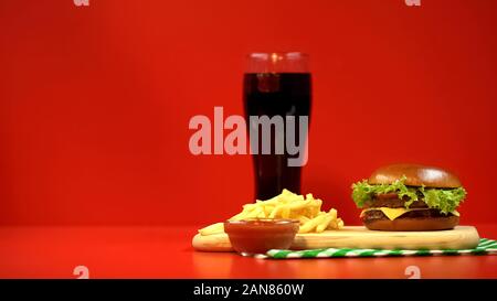 Hamburger frites et ketchup isolé sur fond rouge, repas à forte teneur en calories Banque D'Images
