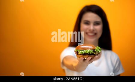 Happy girl montrant hamburger à l'appareil photo, client satisfait de fast food restaurant Banque D'Images