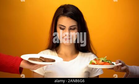 Jeune fille de choisir entre les escalopes et salade végétarienne, choix compliqué Banque D'Images