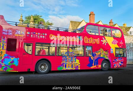 Hop-on hop-off open top ville double decker bus voir peint avec des couleurs criardes en dehors de Trinity College à l'université d'Oxford, en Angleterre. Banque D'Images