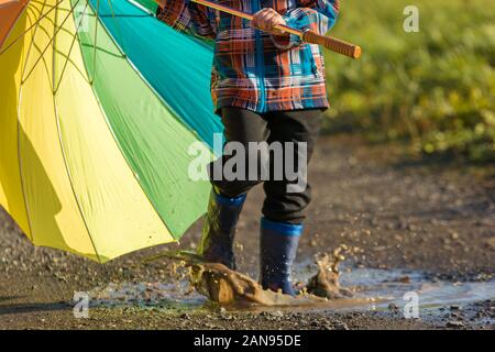 L'enfant joue avec un parapluie coloré dans une flaque Banque D'Images