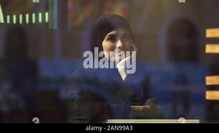 Belle dame musulmane réfléchie assis dans cafe wearing hijab en attente de commande Banque D'Images