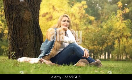 Pretty woman sitting on plaid en vertu de l'arbre dans le parc de l'automne, ce qui pose pour l'appareil photo Banque D'Images